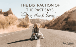 The Distraction of the Past Says, "Stay Stuck Here" | woman sitting in middle of road with mountains behind her