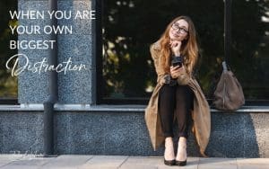 When You Are Your Own Biggest Distraction | woman sitting on ledge with phone in one hand, chin in the other hand while looking up