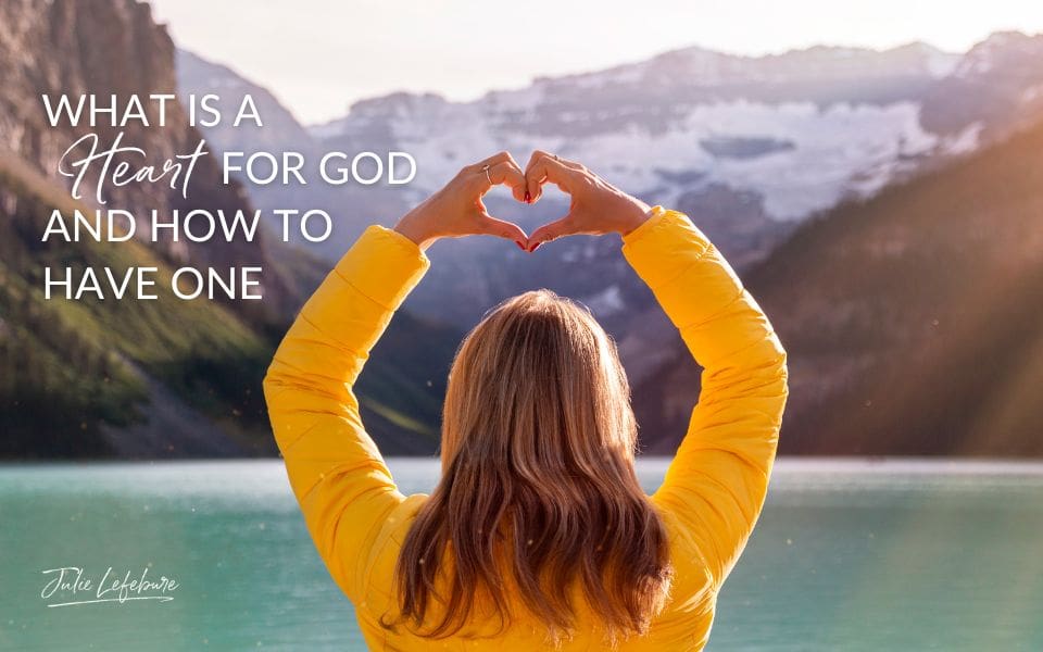 What Is a Heart for God and How to Have One | woman in gold sweater standing on lake shore holding up heart hands